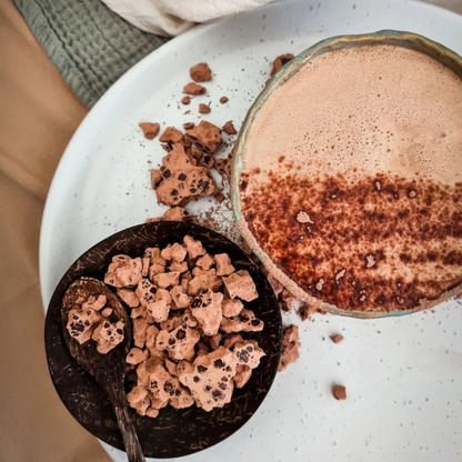 Cup of hot cacao with cacao powder and cacao beans on a white plate.