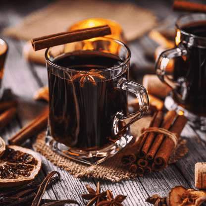 Clear glass mug filled with dark liquid, surrounded by cinnamon sticks and star anise on a wooden surface.